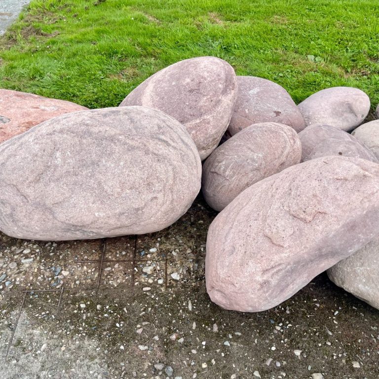 Große Auswahl an grabmalgeeigneten Findlinge Mischung aus großen, glatten Steinen in verschiedenen Formen auf grünem Gras.