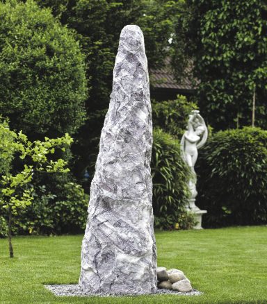 Handgefertigter weißer Marmor-Monolith als Solitär auf einer Rasenfläche.“